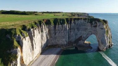Aerial perspective of magnificent Etretat chalk cliffs natural arches and a vibrant green golf course overlooking the clear blue ocean in France.
