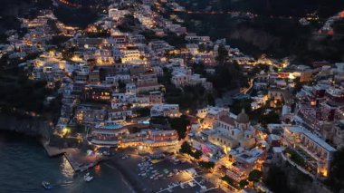 Positano Italys ikonik kıyı kasabası karanlık akşamı aydınlatıyor. Binalar ve sokaklar, sakin körfeze bakan yamaçta parlıyor..