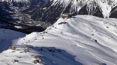 Kayakçı Chamonix Fransa 'da karlı bir dağ yamacından inen izler bırakıyor. Aşağıdaki dağ kulübesi ve vadi kasabası açık bir kış gününde görülebilir..