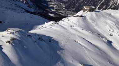Kayakçı karla kaplı bir dağdan yeni izler bırakarak iner. Chamonix Fransa 'da açık gökyüzünün altında bir bina bulunur..