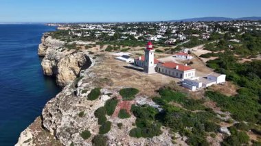 Farol de Alfanzina deniz fenerinin ve Algarve Portekiz 'deki engebeli sahil kayalıklarının havadan görünüşü. Güneş ışığı mavi okyanus suyunu ve manzarayı aydınlatır.