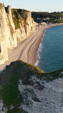 Etretat Fransa 'nın panoramik manzarası. Görkemli beyaz tebeşir kayalıkları yumuşak altın ışıkla yıkanmış sakin bir çakıl taşı plajının üzerinde kule gibi..