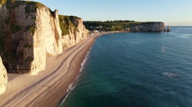 Etretat Fransa 'nın hava keşfi. Görgü tanığı beyaz tebeşir uçurumları çakıl taşı plajı ve mavi deniz ılık altın saat ışığı altında yıkandı..