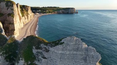 İkonik beyaz tebeşir kayalıklarının panoramik manzarası ve Etretat Fransa 'da uzun çakıllı bir plaj. Sahne, sıcak altın saat ışığıyla aydınlatılır..