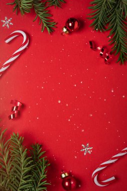 Kırmızı arka planda kırmızı parıltılı süslemeleri olan Noel ağacı dalları çerçevesi. Mutlu Noeller ve mutlu yıllar tebrik kartı. Xmas ve kış tatili. Noel zamanı, üst manzara