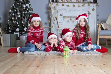 Noel Baba şapkalı dört çocuk yeni yıl süslenmiş şöminesinin yanında oturuyor. Xmas kutlama kartı. Tatil selamlaması. 