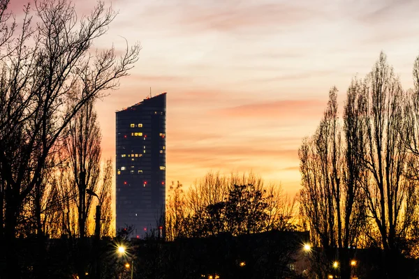 Skyscraper Building With Trees Against Orange Sky At Sunset. Urban Architecture Evening Skyline