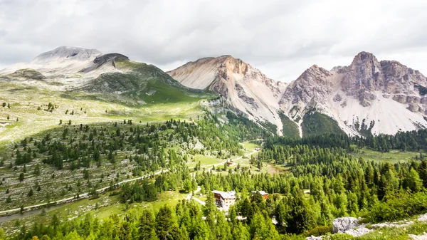 在被群山和雪景环绕的绿色山谷中，可欣赏到高山小屋的全景 — 图库照片