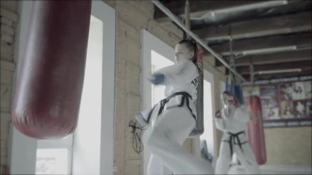 Duas meninas de Taekwondo treinam para um chute no saco de perfuração — Vídeo de Stock