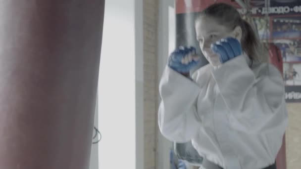 Девушка-тхэквондистка медленно ходит на тренировках с боксёрской сумкой в спортзале — стоковое видео