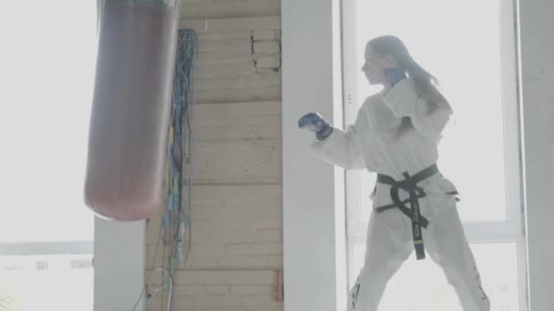 Taekwondo-Mädchen trainiert in Zeitlupe mit Boxsack in der Turnhalle — Stockvideo