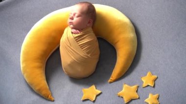 Yeni doğmuş, örülmüş takım elbiseli bir erkek bebek, sarı ayda, sarı yıldızların yanında, örülmüş battaniyelerin üzerinde uyur.