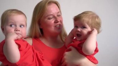 Güzel genç anne ikiz kızlarını kucağında tutuyor.