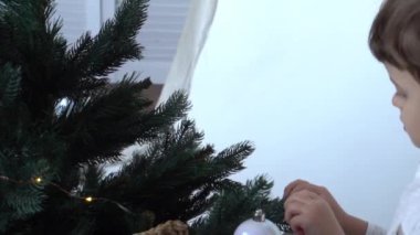Yavaş hareket eden küçük çocuk süslü Noel ağacının yanında gömlek giyiyor.