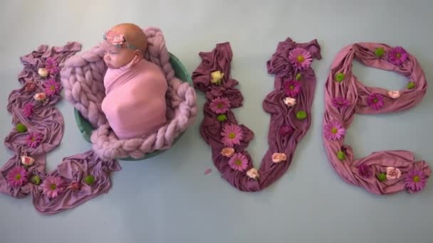 生まれたばかりの赤ちゃんを背景に白い花を咲かせたピンクの愛という言葉 — ストック動画