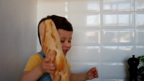 戴着厨师帽子的可爱男孩坐在厨房里 把百吉饼包放在他的脸旁边 — 图库视频影像