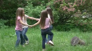 Bir grup çocuk parkta yeşil çimlerde el ele tutuşup dans ediyor. 