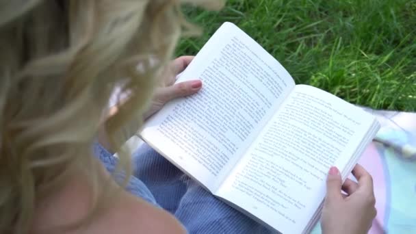 Κορίτσι Κάθεται Στο Γρασίδι Στο Πάρκο Και Διαβάζοντας Ένα Βιβλίο — Αρχείο Βίντεο