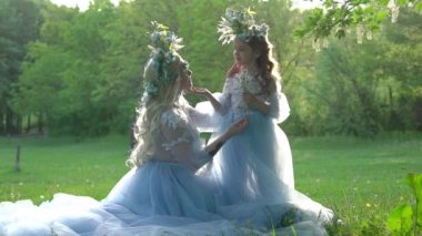 Zarif mavi elbiseli güzel anne ve kız çimlerin üzerinde oturuyor. 