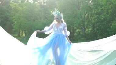 Beyaz çiçeklerden bir çelengi olan genç bir kadın. Mavi elbise rüzgarda dalgalanıyor