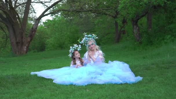 美丽的母亲和女儿穿着雅致的淡蓝色衣服坐在草地上 — 图库视频影像