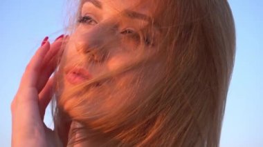 Deniz kıyısında kırmızı elbiseli bir kız kameranın dalgalanan saçlarına bakıyor.