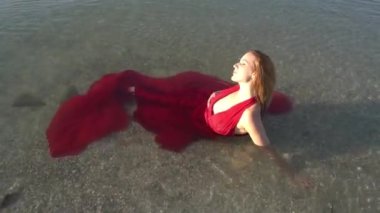 Yazın kırmızı uzun bir elbiseyle denizde yüzen bir kadın.