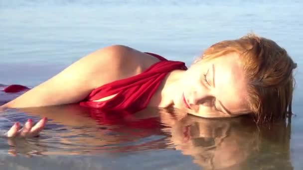 年轻快乐的女人穿着红色的衣服躺在海滩上享受夏日的早晨 — 图库视频影像