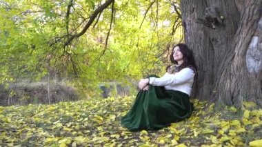 Güzel bir sonbahar parkında bir ağacın altında rüya gibi oturan güzel bir kadın..