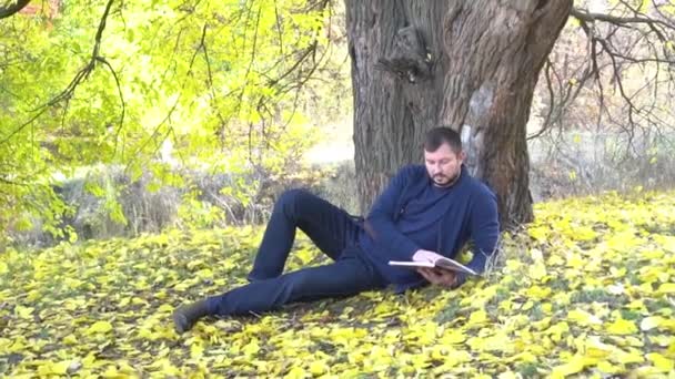 Herbst Park Mann Sitzt Unter Einem Baum Und Liest Buch — Stockvideo