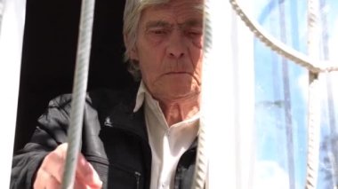 Yaşlı adam pencerenin yanında su içiyor. Bir şey hakkında düşünüyor.