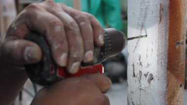 Tanınmayan bir adam Neiva, Huila, Kolombiya 'daki bir döşeme atölyesinde kablosuz bir matkapla duvara delik açıyor. Nesne ve endüstri kavramı