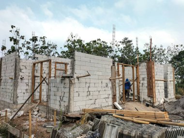 Arkaplan olarak parlak mavi gökyüzüne karşı hafif beton blokları, yapı iskelesi ve güçlendirme çubukları olan ev inşaatı.