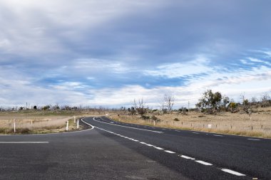 Country main road, at intersection, fading into the distance on a cloudy, blue sky day clipart