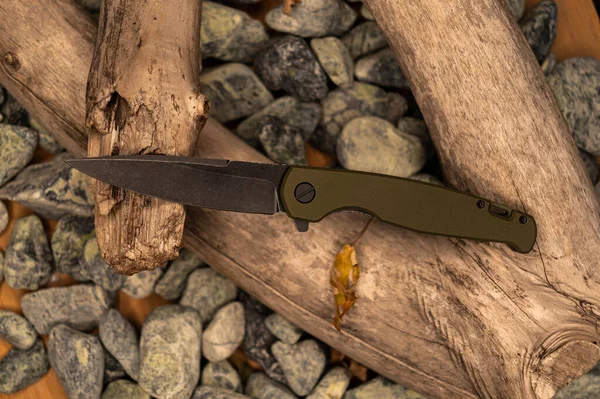 Pocket folding knife with olive handle and black blade. Flat lay. Stones and wood.