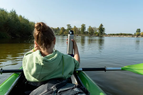 La fille dans le bateau tient un thermos pour le thé. Rafting sur la rivière avec un thermos. — Photo