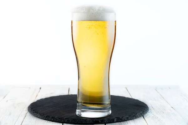Ein Glas leichtes Bier mit Schaum. Glas auf einem schwarzen Tablett. — Stockfoto