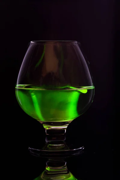 A transparent glass goblet with a green substance. A bright green substance in a glass. Vertical frame.