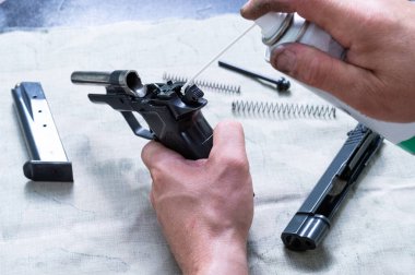 Silah ustası tabancanın mekanizmasını yağlar. Bir pipetle yağlama enjeksiyonu. Usta bir silah ve yağ spreyi tutuyor..
