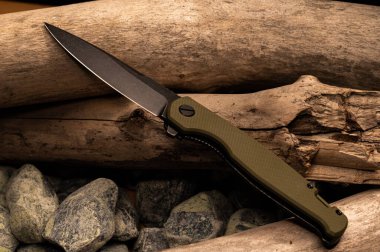 Tahta ve taşlarda keskin, dar bir bıçak. Kütüğün üzerinde çakı. Taşların ve odunların arka planı.