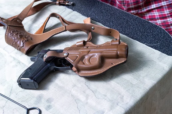 A pistol in a leather holster. The gun is on the table. Top.