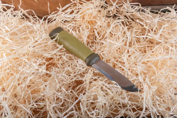 Tourist knife with a fixed blade in the hay. Knife lying in wood shavings. Knife thrown into shavings.