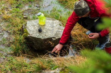 Su birikintisinde bir adam su alıyor. Su birikintisinden su iç. Çimlerden su çekin. Gün ışığı.