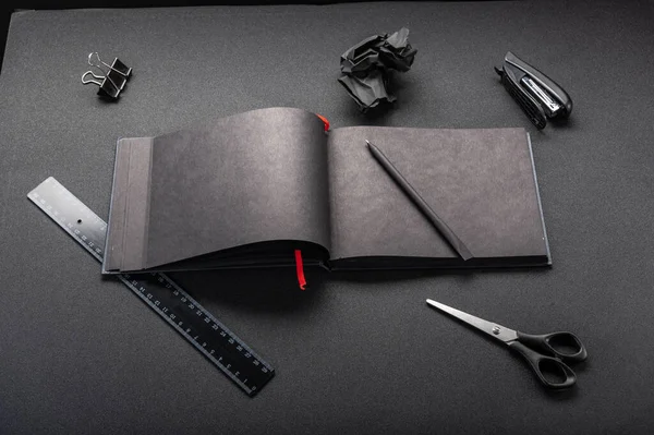 Black office on a black table. Black notebook and stationery. Black office supplies. Top view at an angle.