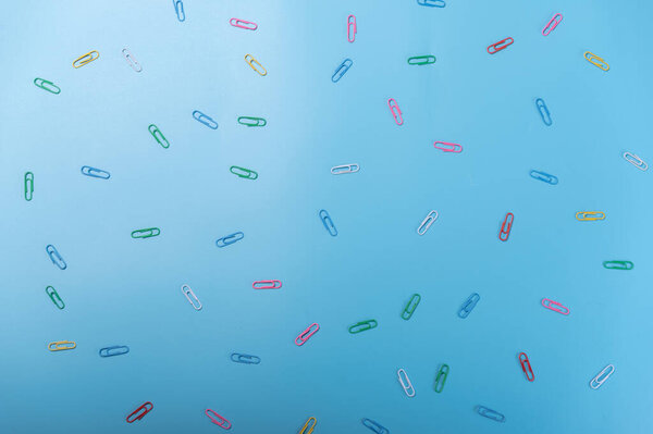 Разноцветные скрепки на синем фоне. Разбросанная скрепка на столе. Топ.
