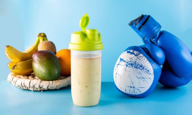 Vitamin proteini spor beslenmesi. Meyvelerden gelen multivitamin yiyeceği. Süt kokteyli ve boks eldivenleri. Mavi arkaplan.