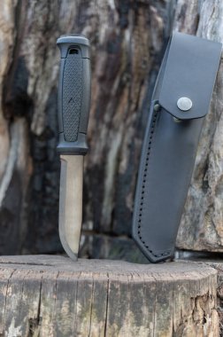 Sabit bıçaklı avcı bıçağı. Bıçak ve deri kılıf. Yanmış odundan bir arka planda bıçak. Dikey çerçeve.