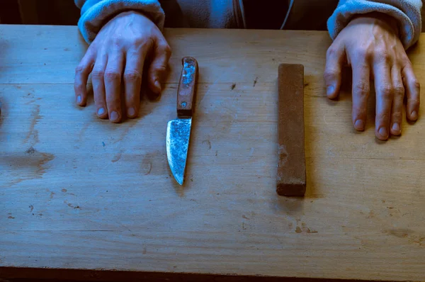 Hands and an old knife. Homemade knife. Old rusty knife and whetstone. Homemade knife restoration. Angle view.
