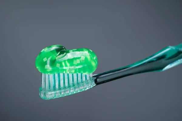 Green toothpaste. Toothpaste on a toothbrush. Toothpaste with additives. Gray background. Toothpaste isolate. Front view.