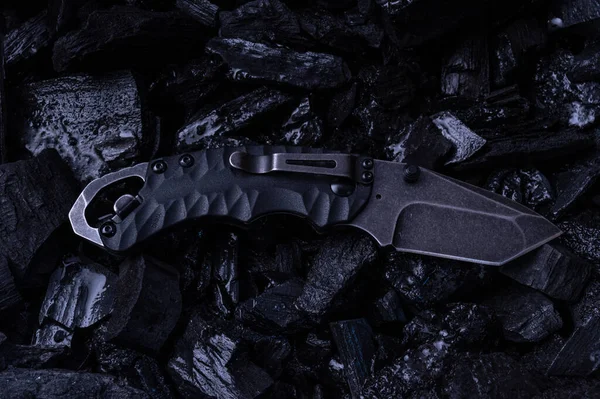 Folding knife with a bottle opener. Knife with a clip for carrying. Black knife on black stones. — Stock Photo, Image